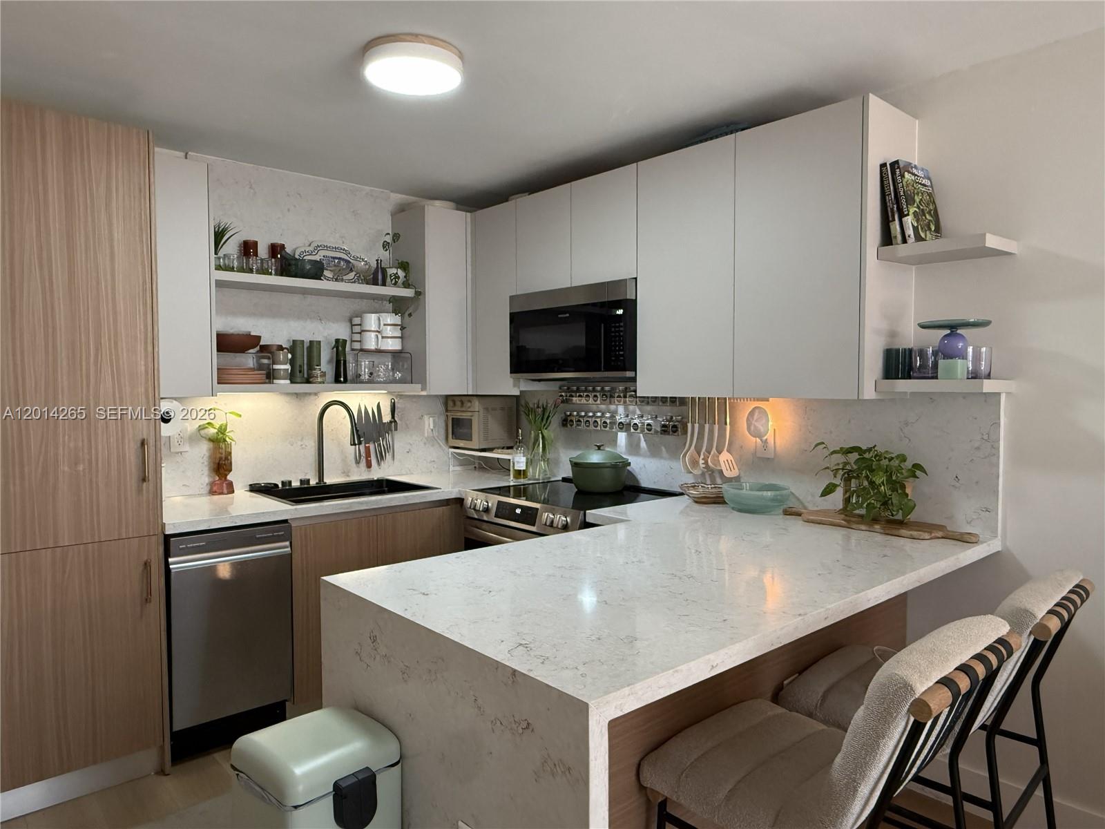 A modern kitchen features white upper cabinets, wood-toned lower cabinets, and a quartz waterfall island — 1666 West Ave # 305, Miami Beach FL 33139, MIAMI BEACH, FL