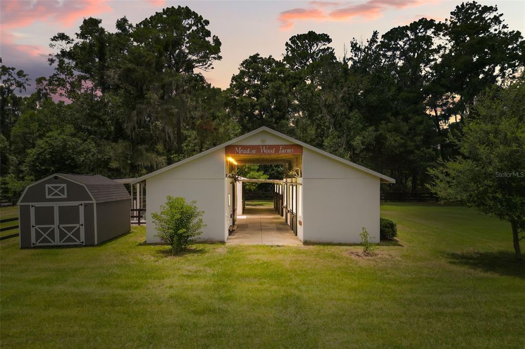 A white horse barn with a sign reading Meadow Wood Farms sits on a lawn — 22 WOOD RIDGE DRIVE, OCALA, FL