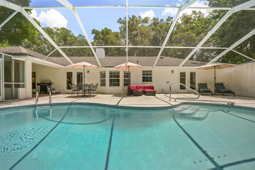 A swimming pool sits on a patio enclosed by a screened lanai behind a house — 22 WOOD RIDGE DRIVE, OCALA, FL