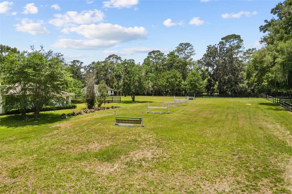 A grassy backyard features several equestrian jumps and a line of mature trees — 22 WOOD RIDGE DRIVE, OCALA, FL