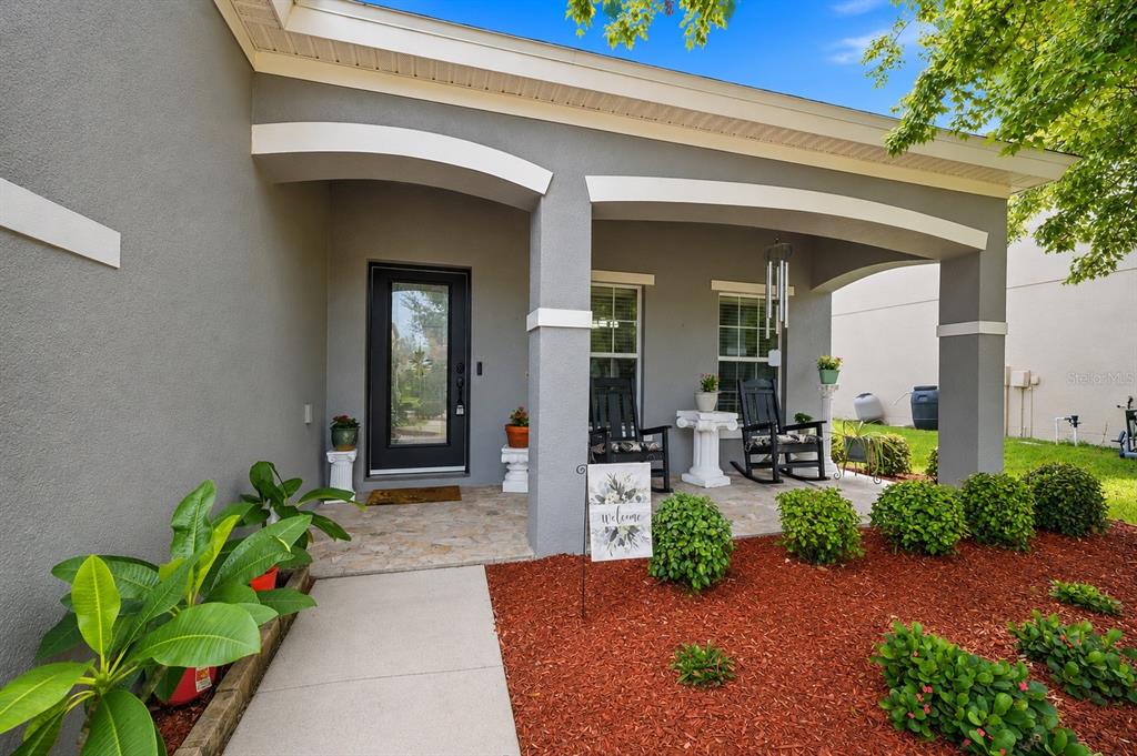 A covered front porch with a stone floor, two rocking chairs, and red mulch landscaping — 2814 MAPLE BROOK LOOP, LUTZ, FL
