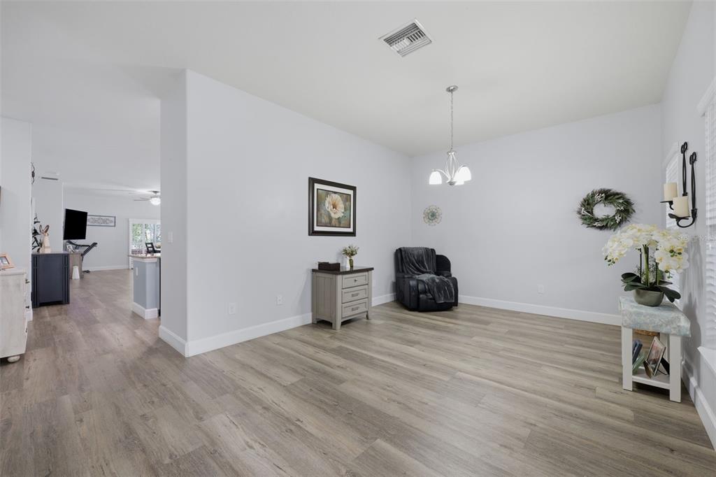 A bright dining room features light wood-look flooring, a central chandelier, and a dark armchair — 2814 MAPLE BROOK LOOP, LUTZ, FL