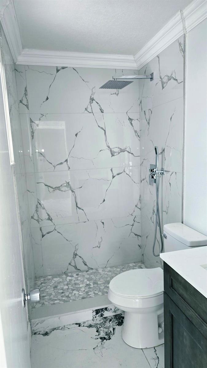 A bathroom features a walk-in shower with marble-patterned tile, a pebble floor, and a toilet — LAUDERHILL, FL