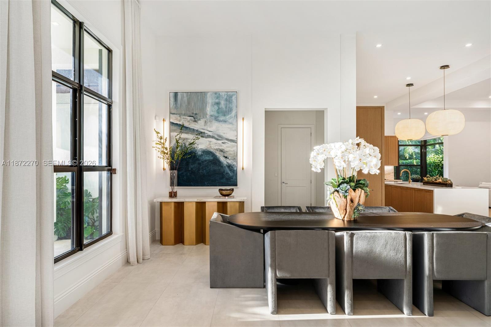 A modern dining room features a dark oval table, gray chairs, and a gold console — 9445 SW 72nd Ct, Pinecrest FL 33156, PINECREST, FL