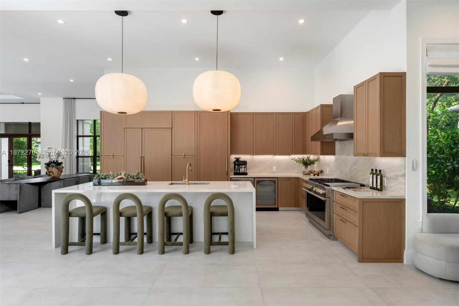 A modern kitchen features light wood cabinetry, a white island with four stools, and pendant lights — 9445 SW 72nd Ct, Pinecrest FL 33156, PINECREST, FL