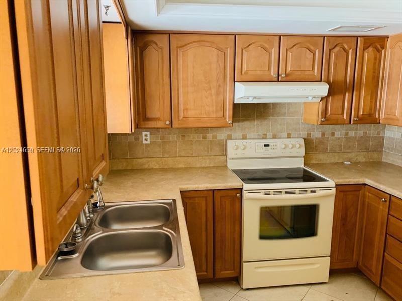 A kitchen features wood cabinets, a double sink, and a white stove with a range hood — 344 SW 1st St # 9, Pompano Beach FL 33060, POMPANO BEACH, FL