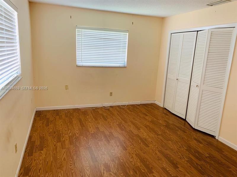 An empty bedroom features light-colored walls, wood-look flooring, a window with blinds, and closet doors — 344 SW 1st St # 9, Pompano Beach FL 33060, POMPANO BEACH, FL