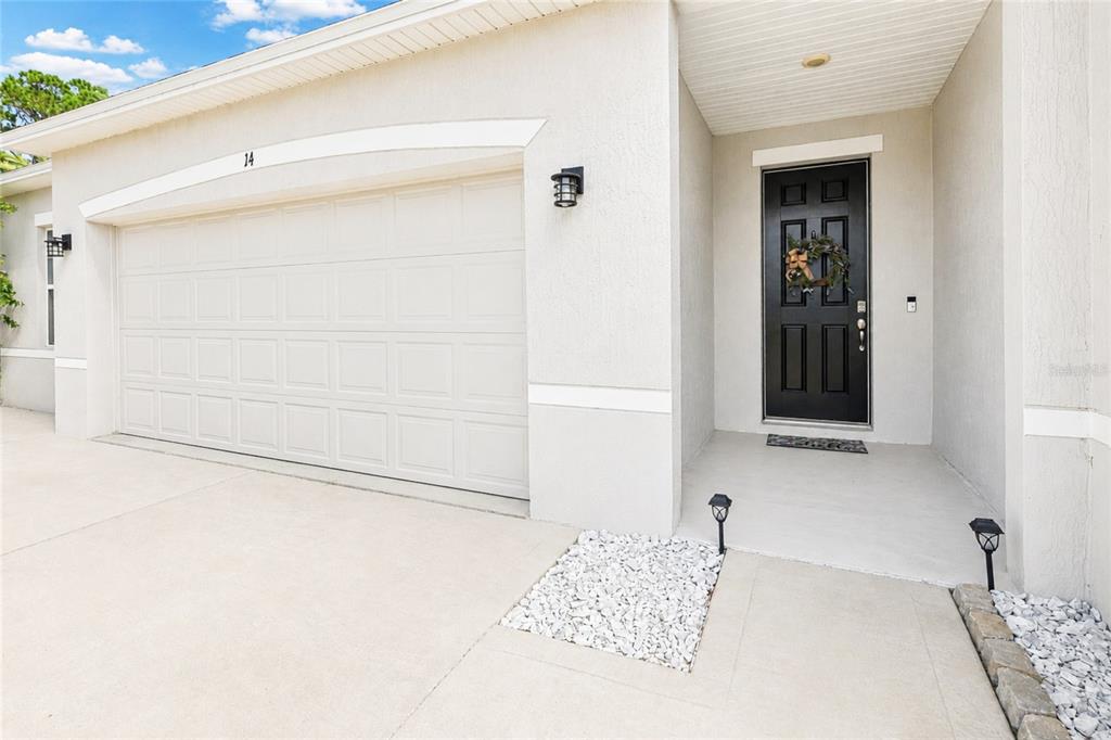 The exterior of a house features a white garage door, a black front door, and gravel — 14 WOODWORTH DRIVE, PALM COAST, FL