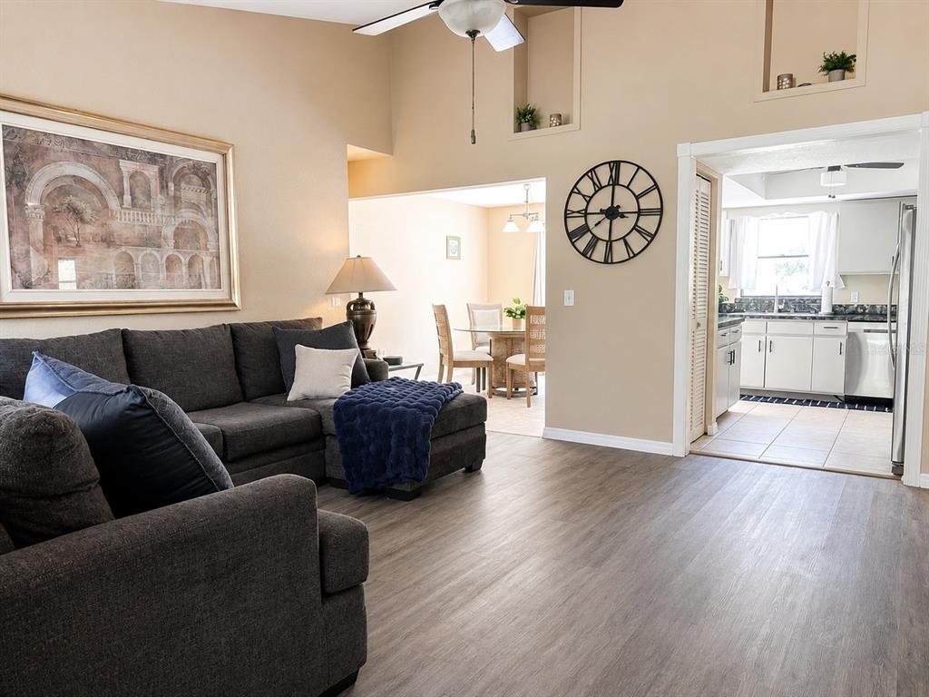 A living room with gray flooring and a sectional sofa opens to a dining area — 307 BARGER DRIVE, PORT CHARLOTTE, FL