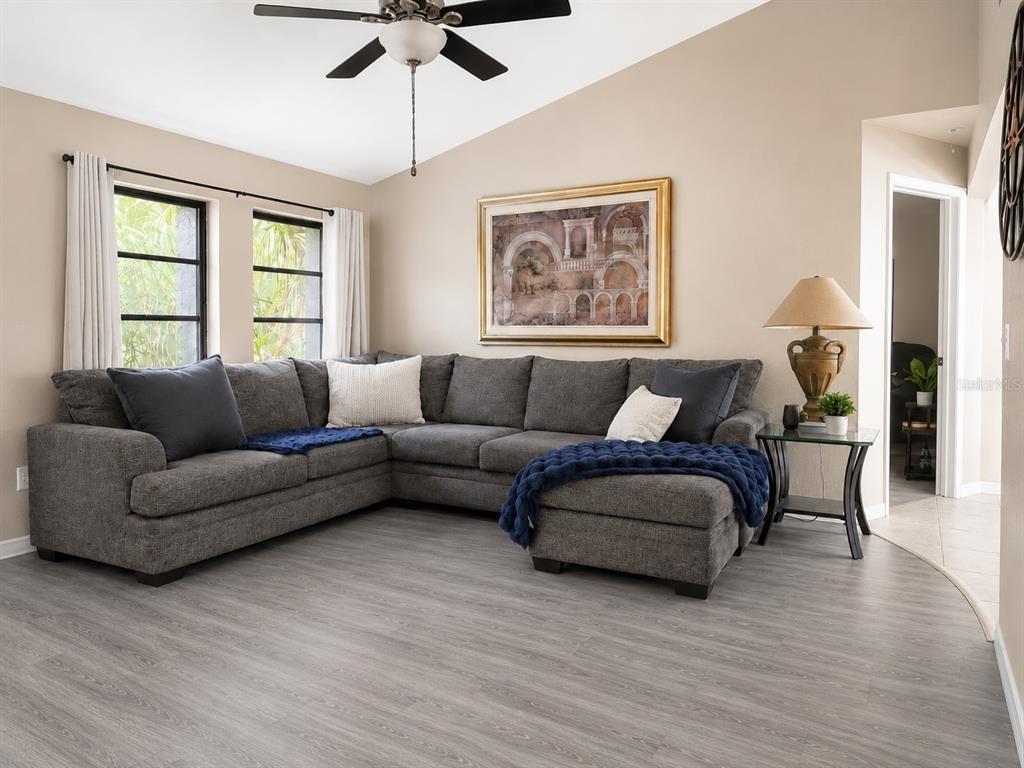 A living room features a gray sectional sofa, wood-look flooring, and a vaulted ceiling — 307 BARGER DRIVE, PORT CHARLOTTE, FL