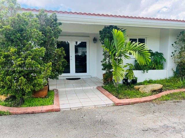 The exterior of a white house features a tiled entryway, double glass doors, and landscaping — 7910 SW 73rd Ct, Miami FL 33143, MIAMI, FL