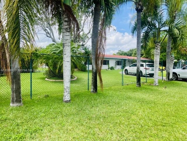 A chain-link fence surrounds a grassy yard with palm trees in front of a house — 7910 SW 73rd Ct, Miami FL 33143, MIAMI, FL