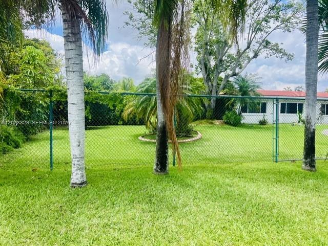 A green chain-link fence separates a grassy yard from a house with a red roof — 7910 SW 73rd Ct, Miami FL 33143, MIAMI, FL