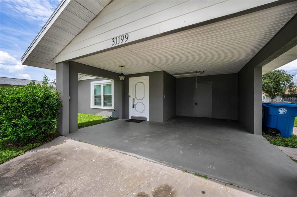 A gray house exterior features a covered carport, a white front door, and a window — 31199 LANCEWOOD DRIVE, BROOKSVILLE, FL