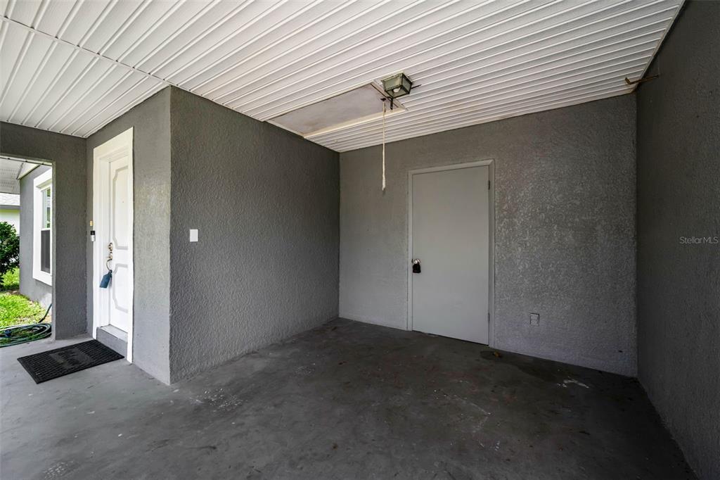 A covered porch features gray stucco walls, a white door, and a ceiling access panel — 31199 LANCEWOOD DRIVE, BROOKSVILLE, FL