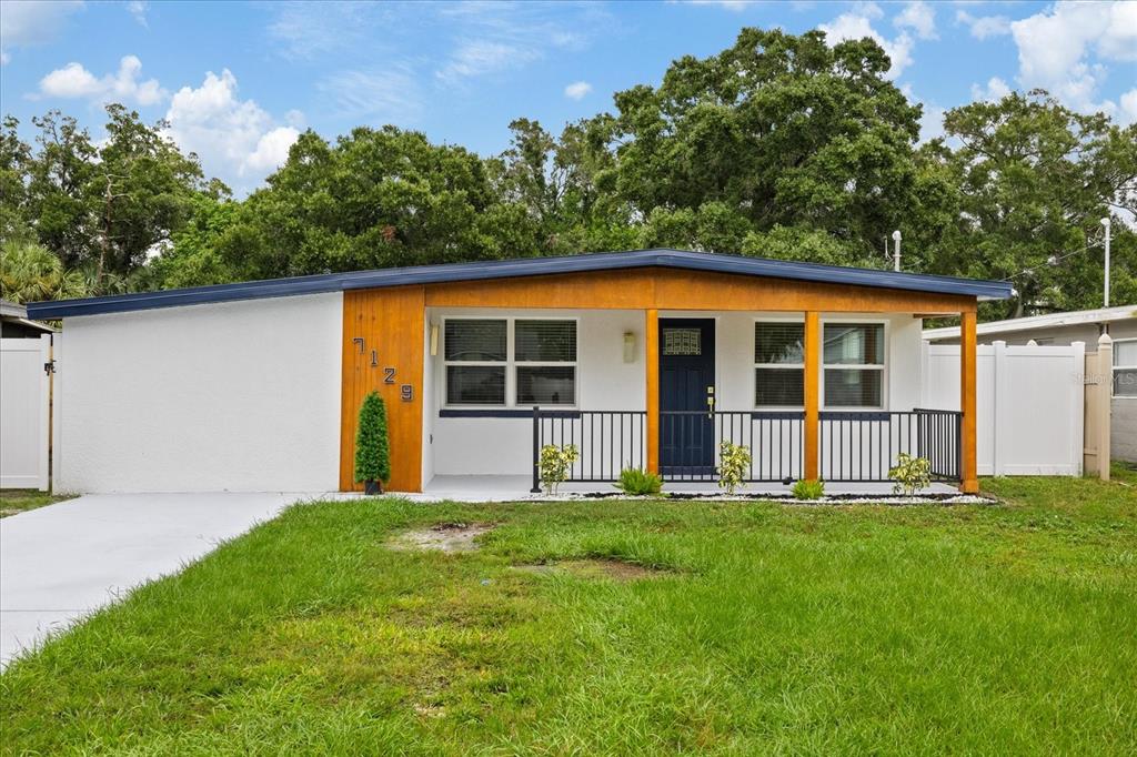 A single-story house with a white exterior, wood-paneled entryway, and a black metal porch railing — 7129 63RD STREET N, PINELLAS PARK, FL