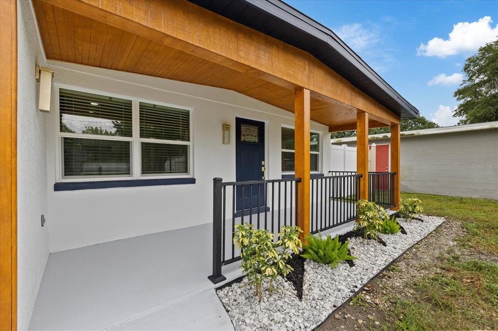 A covered front porch with wood ceiling beams, black railings, and a blue front door — 7129 63RD STREET N, PINELLAS PARK, FL