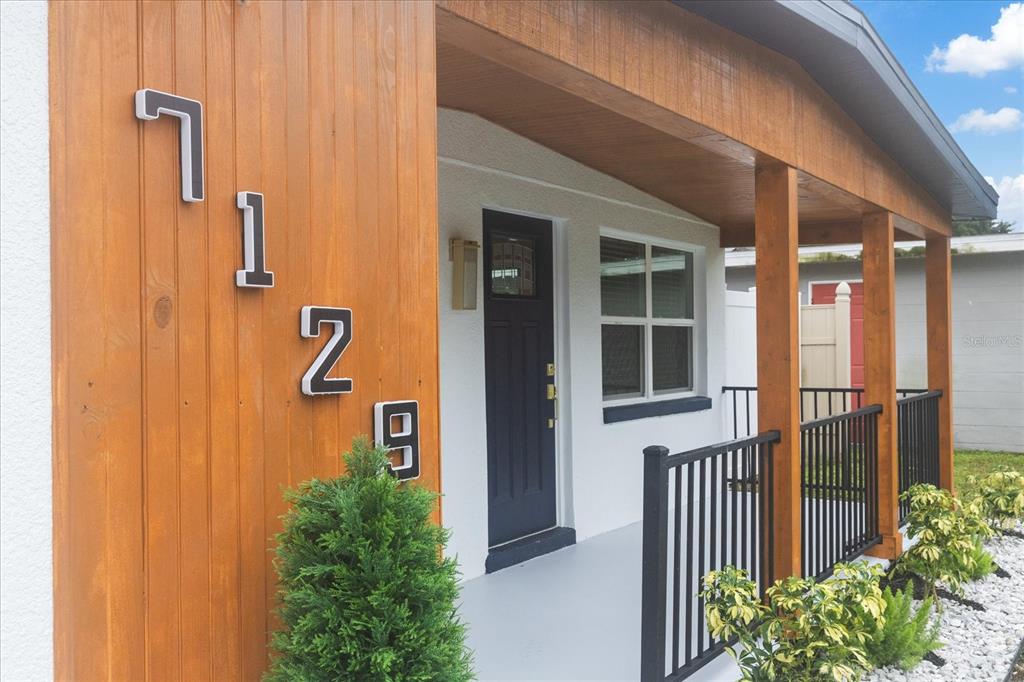 The exterior of a house features a wood-paneled wall with house numbers and a porch — 7129 63RD STREET N, PINELLAS PARK, FL