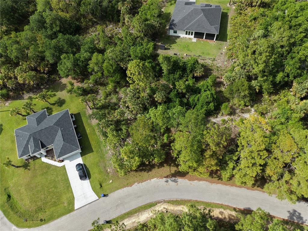 An aerial view shows two houses surrounded by dense trees along a curved paved road — DE BRITA ROAD, NORTH PORT, FL