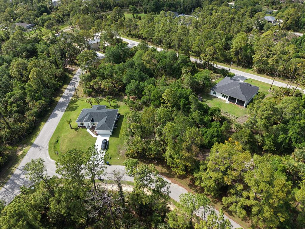 An aerial view shows two houses surrounded by dense trees and paved roads — DE BRITA ROAD, NORTH PORT, FL