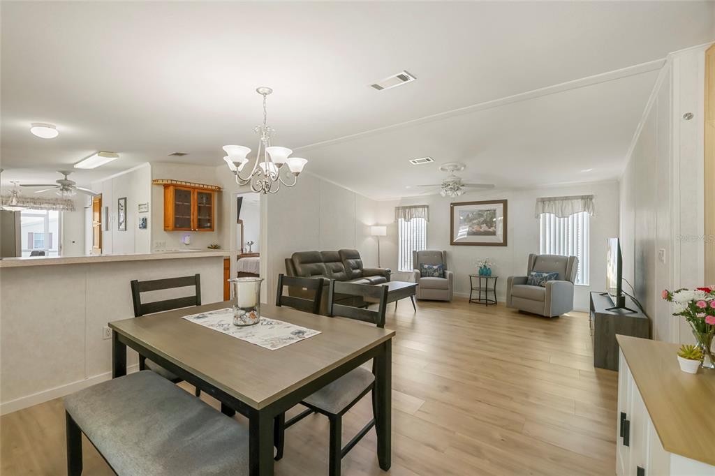 An open-concept living and dining area features light wood flooring, a chandelier, and neutral walls — 2927 COQUINA ESPLANADE, PUNTA GORDA, FL