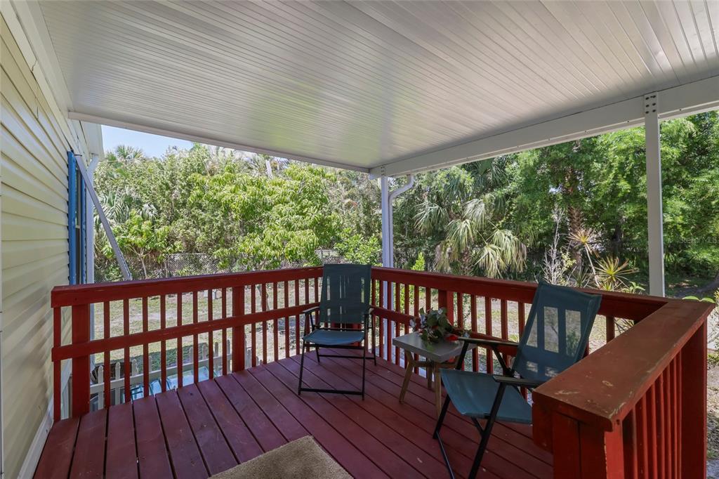 A covered wooden deck features red railings, two folding chairs, and a small side table — 2927 COQUINA ESPLANADE, PUNTA GORDA, FL
