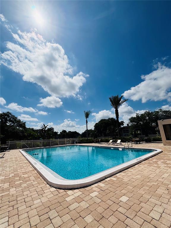 A rectangular swimming pool is surrounded by a paved patio under a sunny blue sky — 10356 CARROLLWOOD LANE UNIT 205, TAMPA, FL