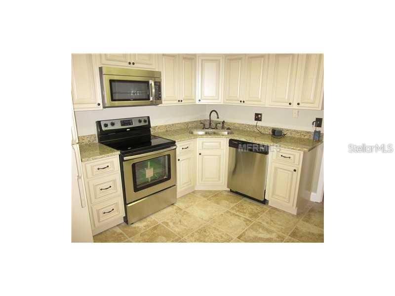 A kitchen features off-white cabinets, stainless steel appliances, granite countertops, and tiled flooring — 10356 CARROLLWOOD LANE UNIT 205, TAMPA, FL