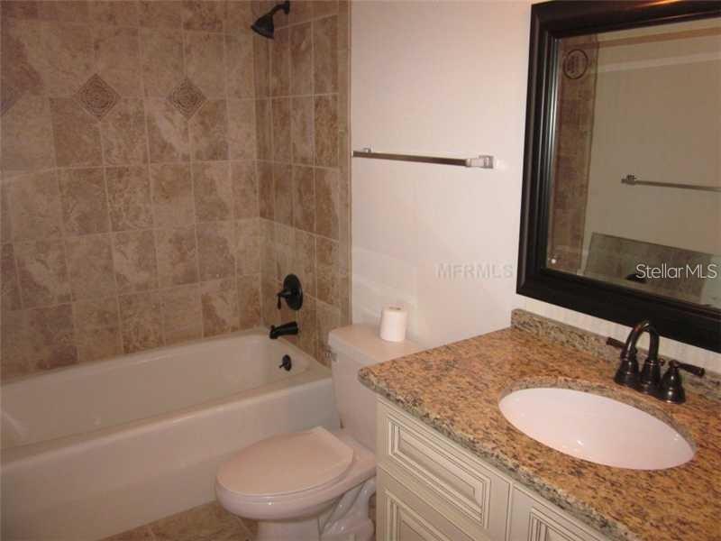 A bathroom features a tiled shower-tub combo, a granite vanity, and a dark-framed mirror — 10356 CARROLLWOOD LANE UNIT 205, TAMPA, FL
