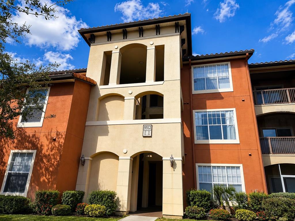 A three-story apartment building exterior features tan stucco, orange walls, and a central entryway — 5512 METROWEST BOULEVARD UNIT 201, ORLANDO, FL