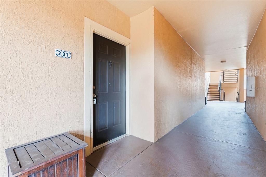 A dark front door with a 201 sign is located in a beige outdoor hallway — 5512 METROWEST BOULEVARD UNIT 201, ORLANDO, FL