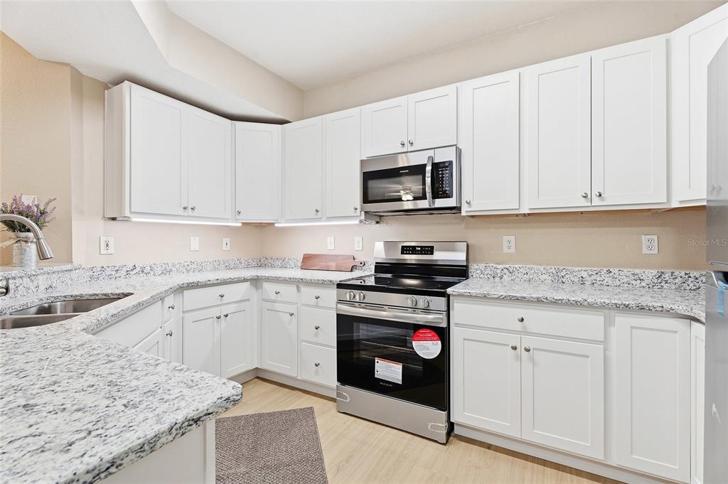 A kitchen features white cabinets, granite countertops, and stainless steel appliances — 5512 METROWEST BOULEVARD UNIT 201, ORLANDO, FL