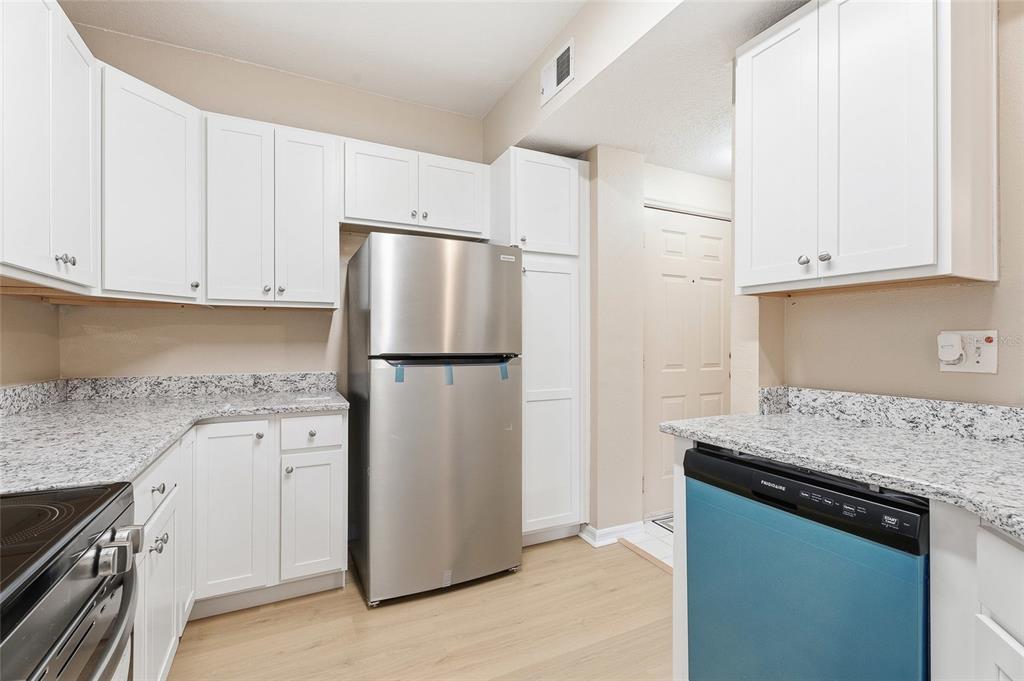 A kitchen with white cabinets, granite countertops, and stainless steel appliances on light wood flooring — 5512 METROWEST BOULEVARD UNIT 201, ORLANDO, FL