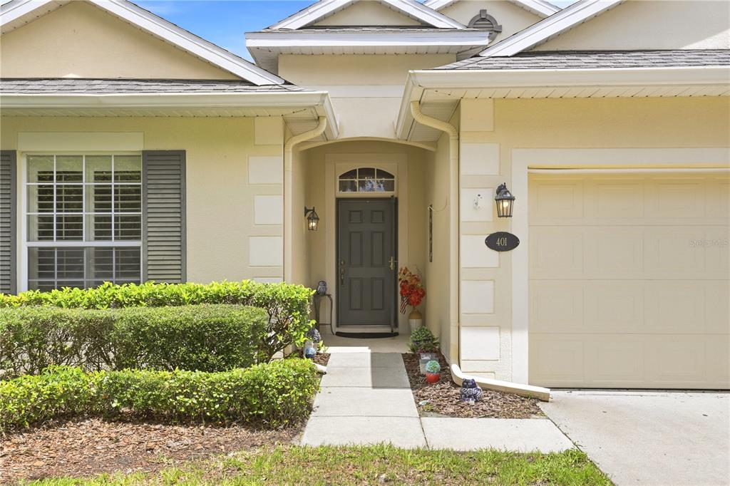 The exterior of a single-story house features a beige facade, a dark door, and a garage — 401 HERON POINT WAY, DELAND, FL