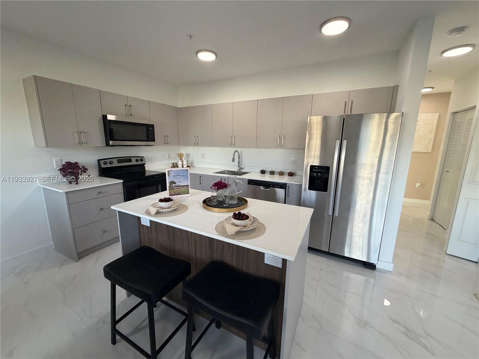 A modern kitchen features light gray cabinets, stainless steel appliances, and a central island — 2308 E 4th Ave # 205, Hialeah FL 33013, HIALEAH, FL
