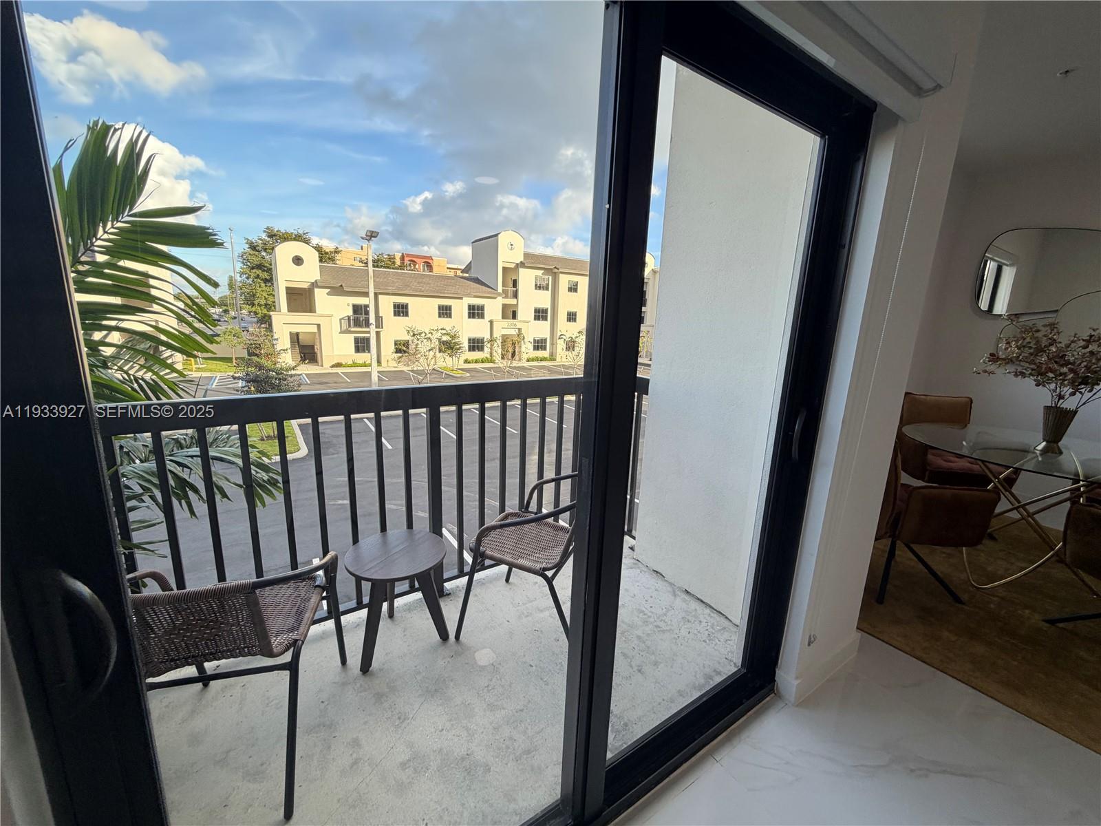 A balcony with two chairs and a small table overlooks a parking lot and building — 2308 E 4th Ave # 205, Hialeah FL 33013, HIALEAH, FL