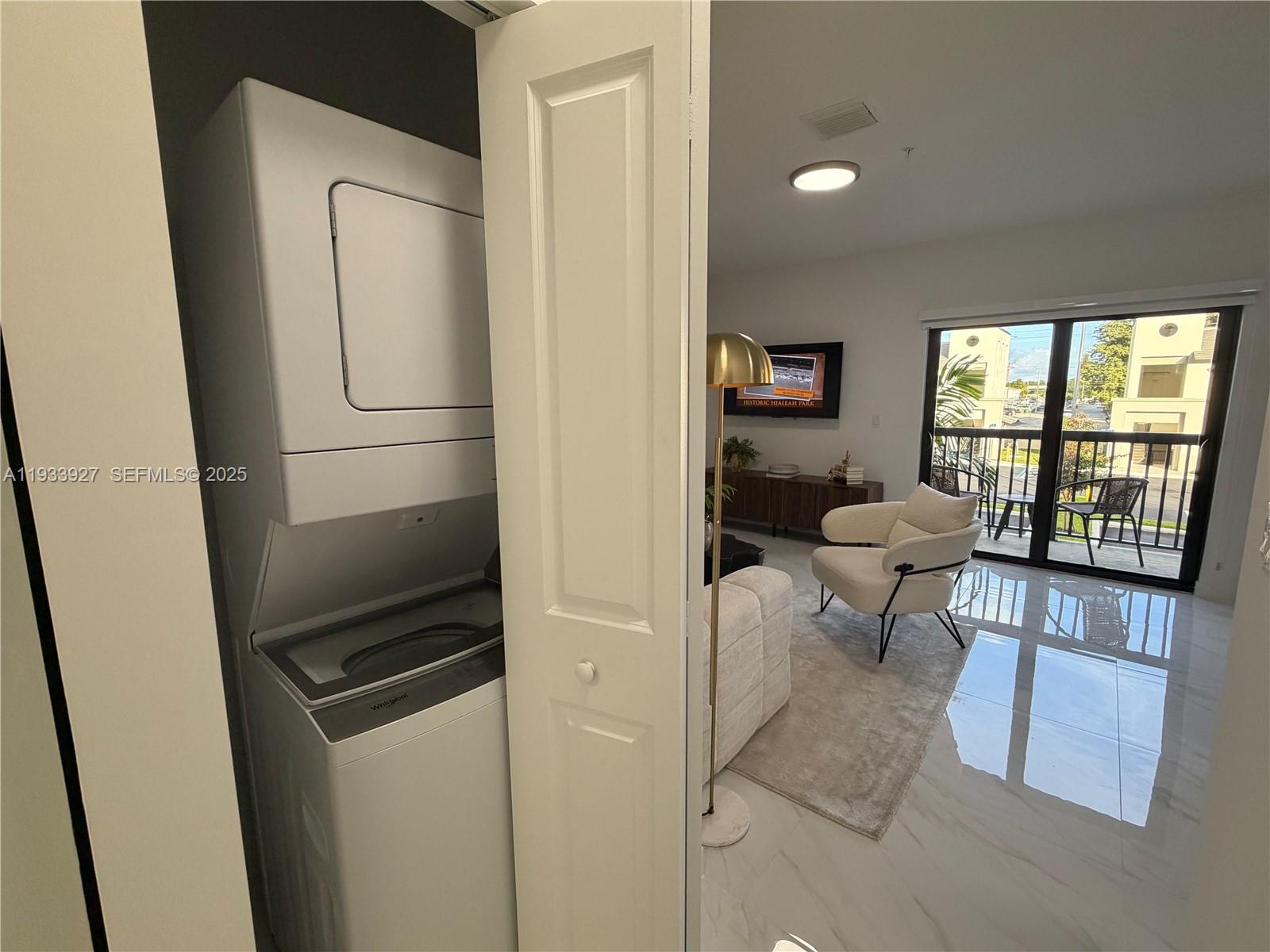 A stacked washer and dryer unit sits in a closet next to a living room — 2308 E 4th Ave # 205, Hialeah FL 33013, HIALEAH, FL