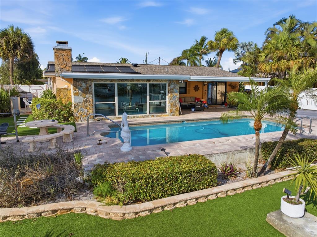 A backyard features a swimming pool, stone-accented house exterior, patio furniture, and palm trees — 412 HERMOSITA DRIVE, ST PETERSBURG, FL
