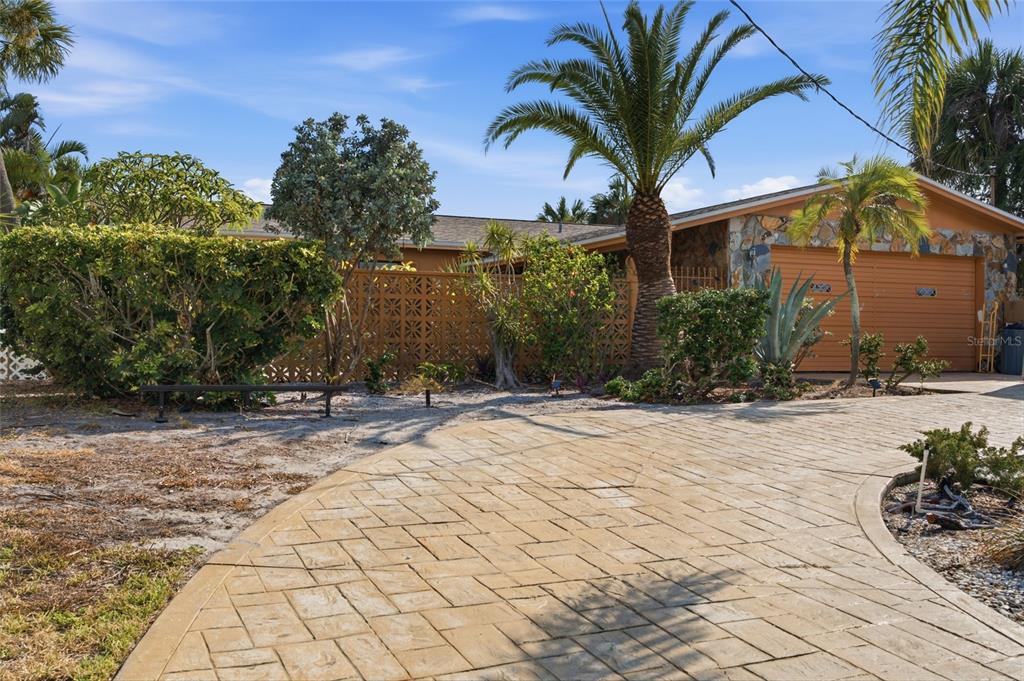 A paved driveway leads to a house with a stone-accented garage and tropical landscaping — 412 HERMOSITA DRIVE, ST PETERSBURG, FL