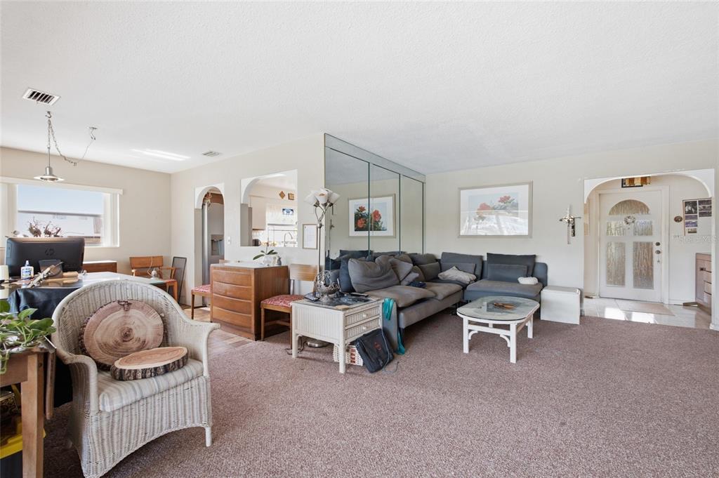A living room with beige carpet, a gray sectional sofa, mirrored walls, and an arched entryway — 412 HERMOSITA DRIVE, ST PETERSBURG, FL