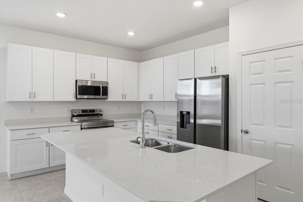 A modern kitchen features white cabinets, stainless steel appliances, and a large quartz-topped island — 155 BOTTLE BRUSH, HAINES CITY, FL