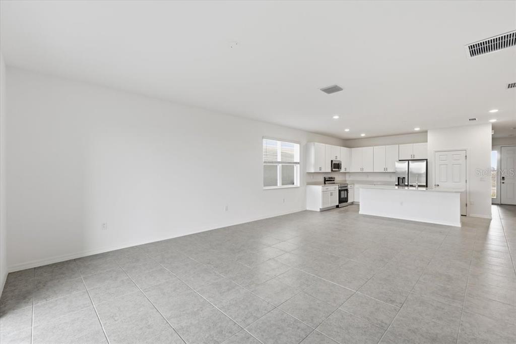 An open-concept kitchen and living area with white cabinets, stainless appliances, and tile flooring — 155 BOTTLE BRUSH, HAINES CITY, FL