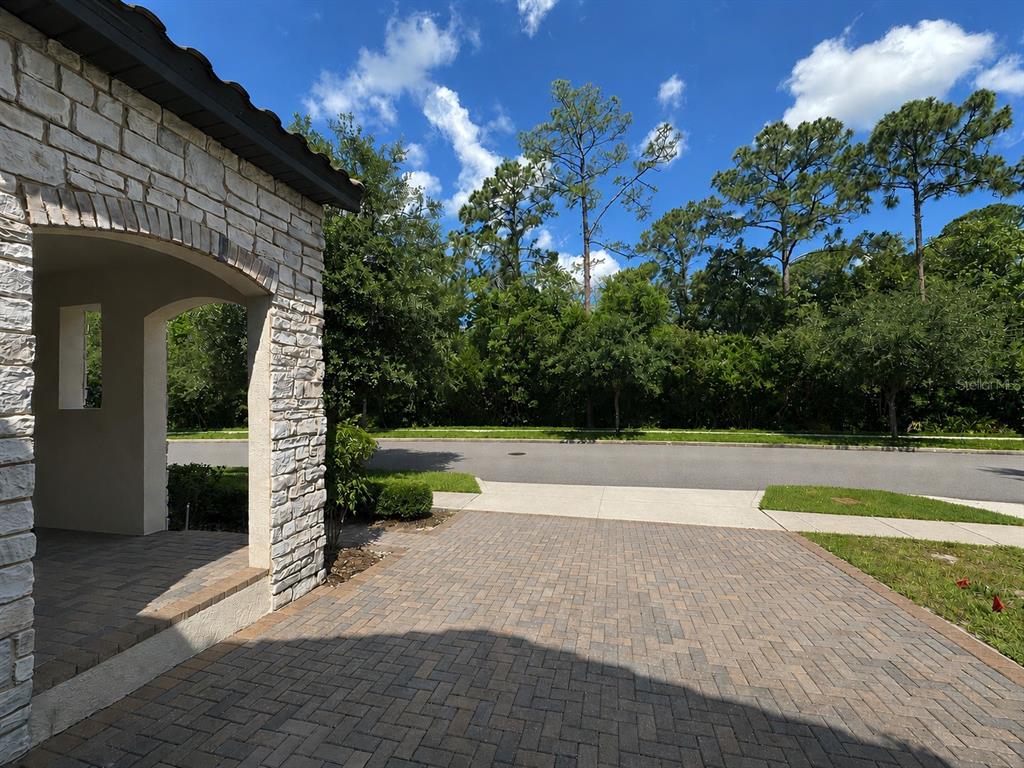 A stone-faced entryway leads to a paved driveway overlooking a quiet street and trees — 8355 TORCELLO ISLE DRIVE, WINDERMERE, FL