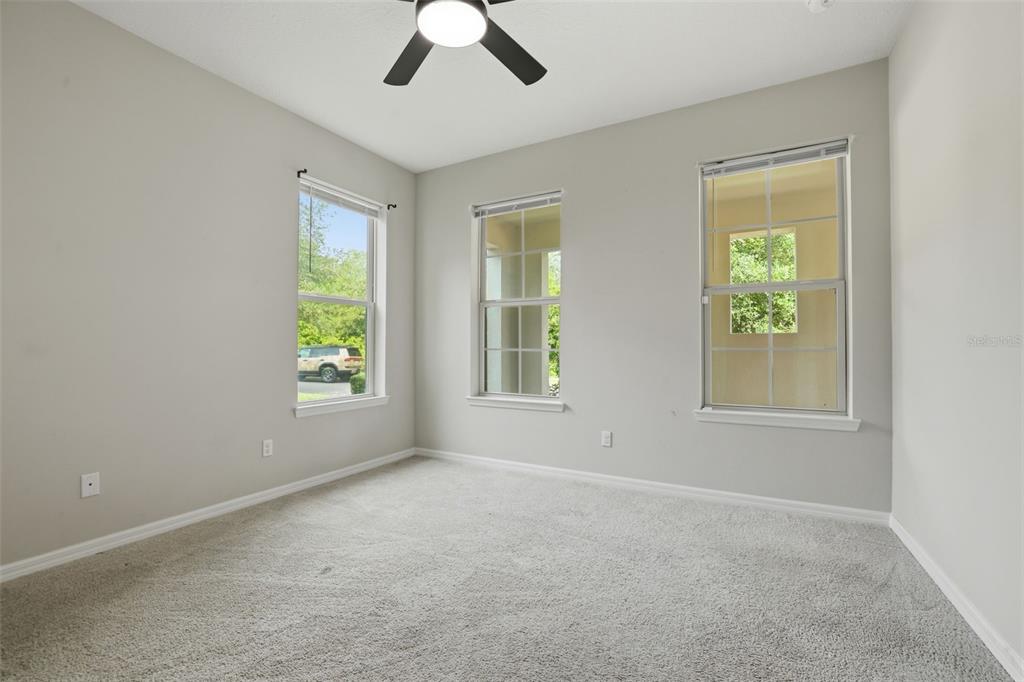 An empty bedroom features light gray walls, carpeted flooring, a ceiling fan, and three windows — 8355 TORCELLO ISLE DRIVE, WINDERMERE, FL