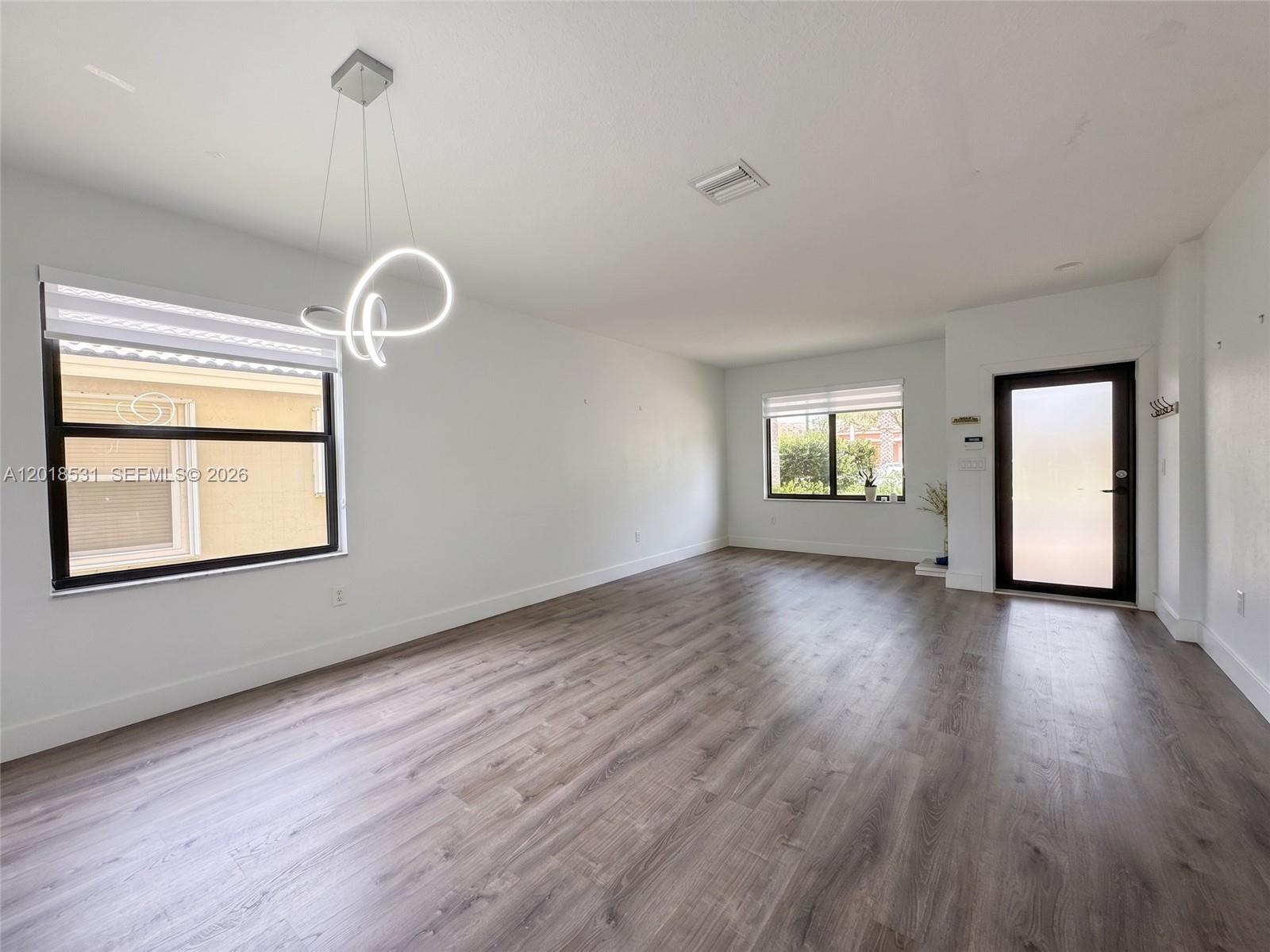 An empty room with wood-look flooring, white walls, a modern light fixture, and two windows — 1575 SE 20th Rd, Homestead FL 33035, HOMESTEAD, FL