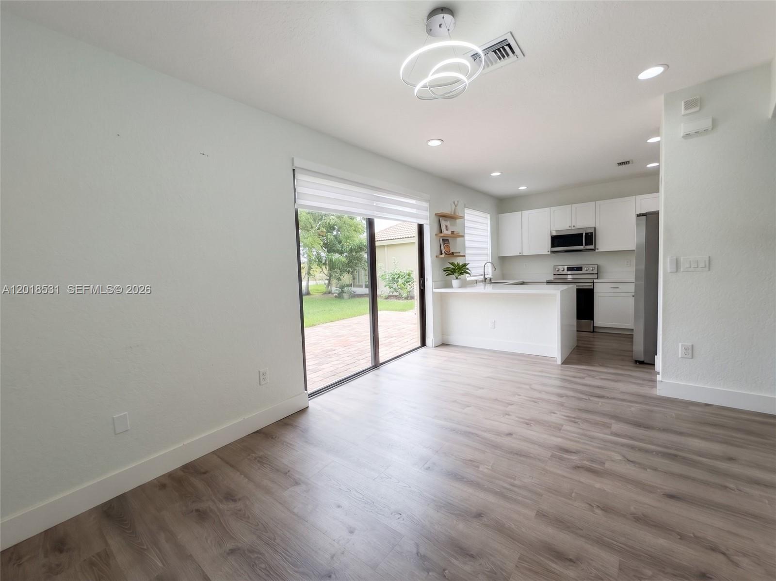 An open-concept kitchen and living area features white cabinetry, light wood-look flooring, and sliding doors — 1575 SE 20th Rd, Homestead FL 33035, HOMESTEAD, FL