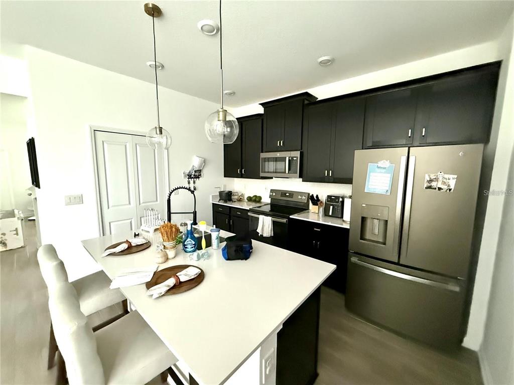 A kitchen features dark cabinets, stainless steel appliances, and a white island with seating — 1796 TOHOQUA BOULEVARD, KISSIMMEE, FL