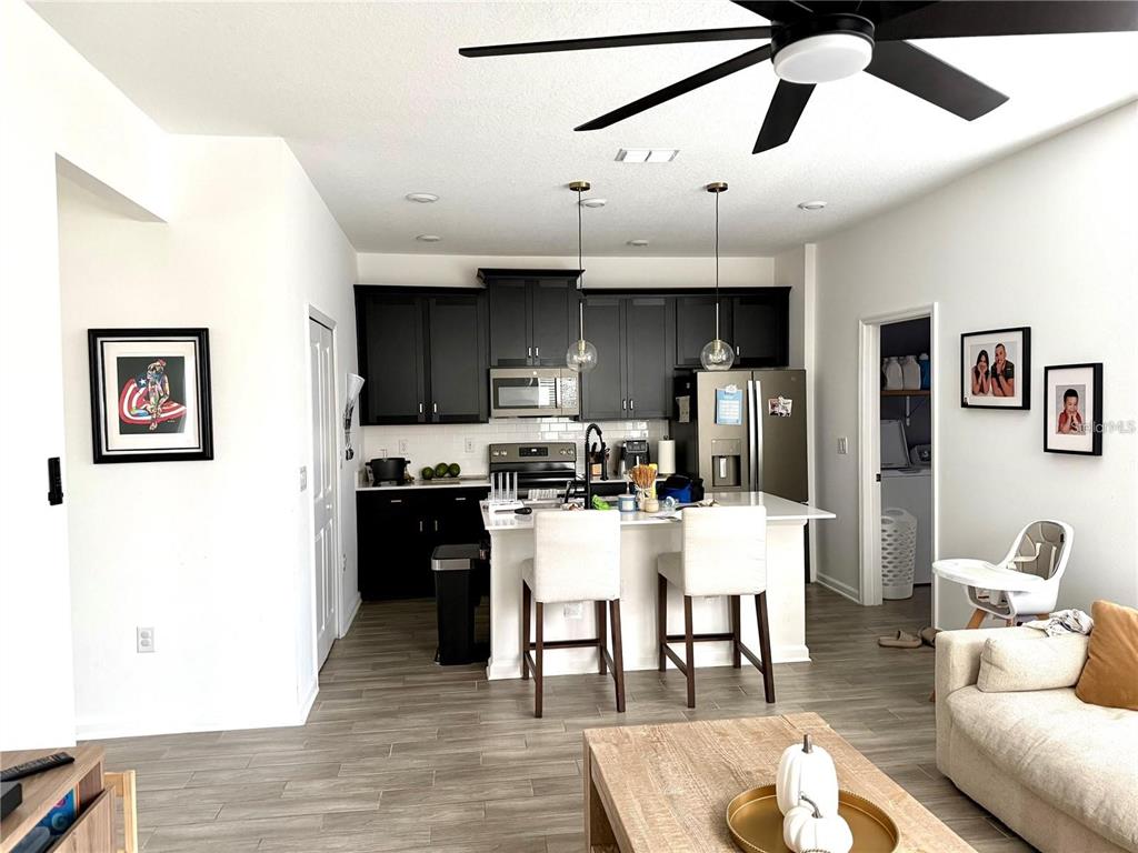 A kitchen with black cabinets, a white island, and stainless steel appliances opens to a living area — 1796 TOHOQUA BOULEVARD, KISSIMMEE, FL