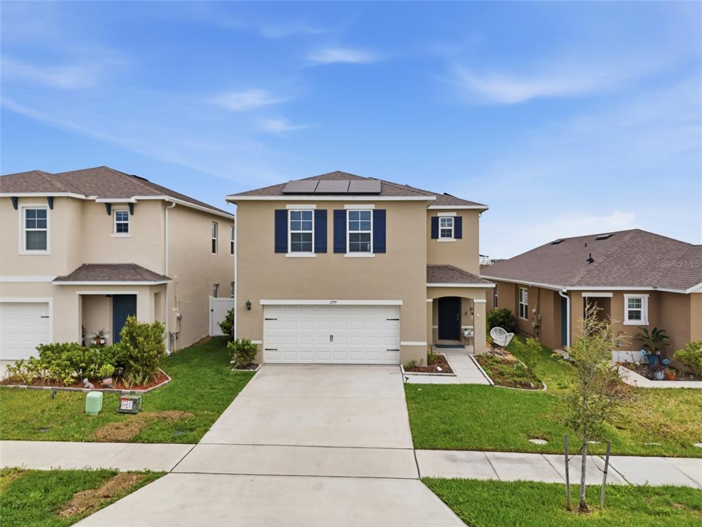 A two-story suburban house with a tan stucco exterior, white garage door, and solar panels — 1777 WALNUT CREEK DRIVE, KISSIMMEE, FL