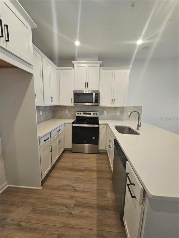 A kitchen features white cabinets, stainless steel appliances, quartz countertops, and wood-look flooring — 11459 SUNSAIL AVENUE, ORLANDO, FL